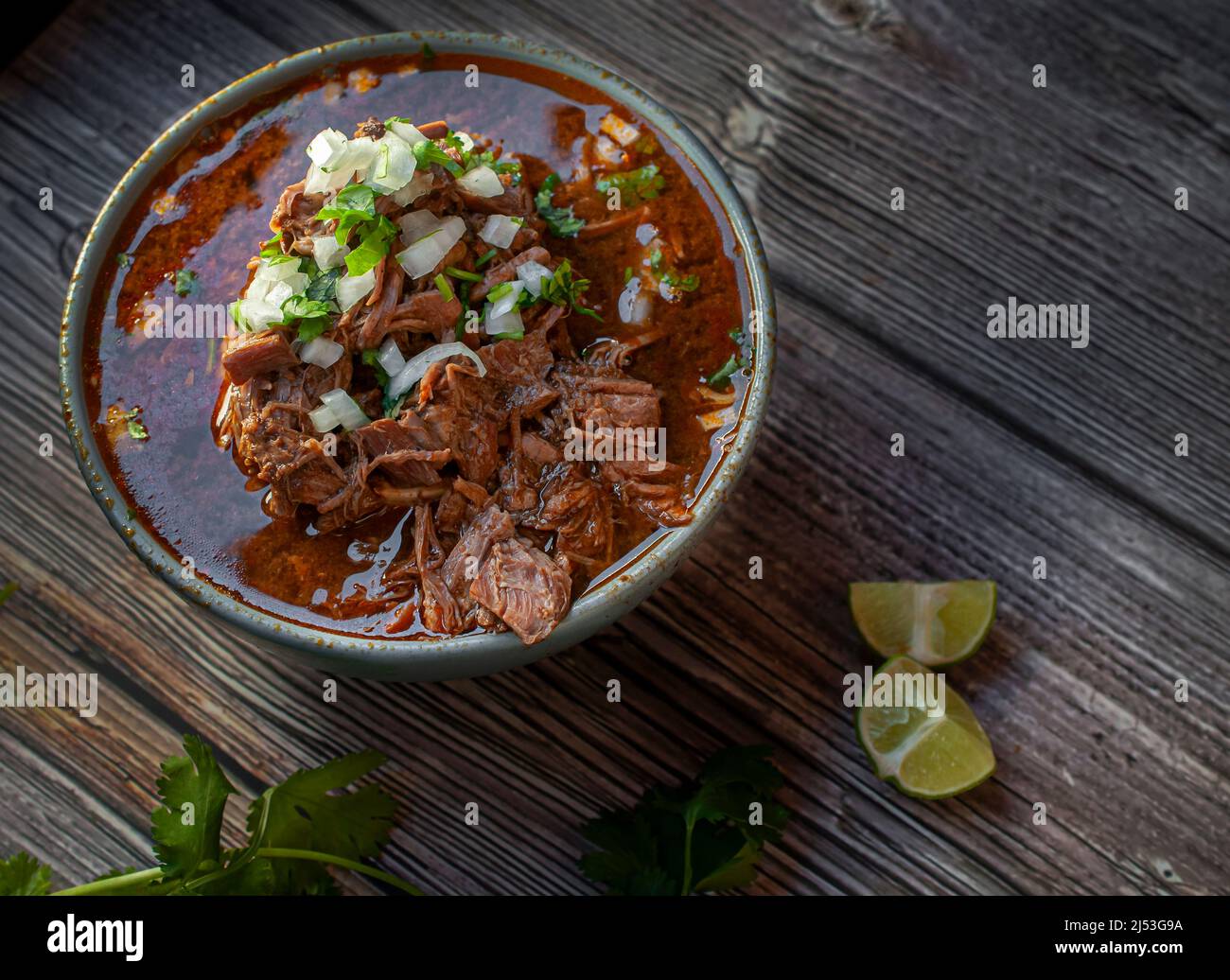 A bowl of BIRRIA or BARBACOA, a traditional Mexican dish with lemons and  cilantro on the side over a wooden table Stock Photo - Alamy