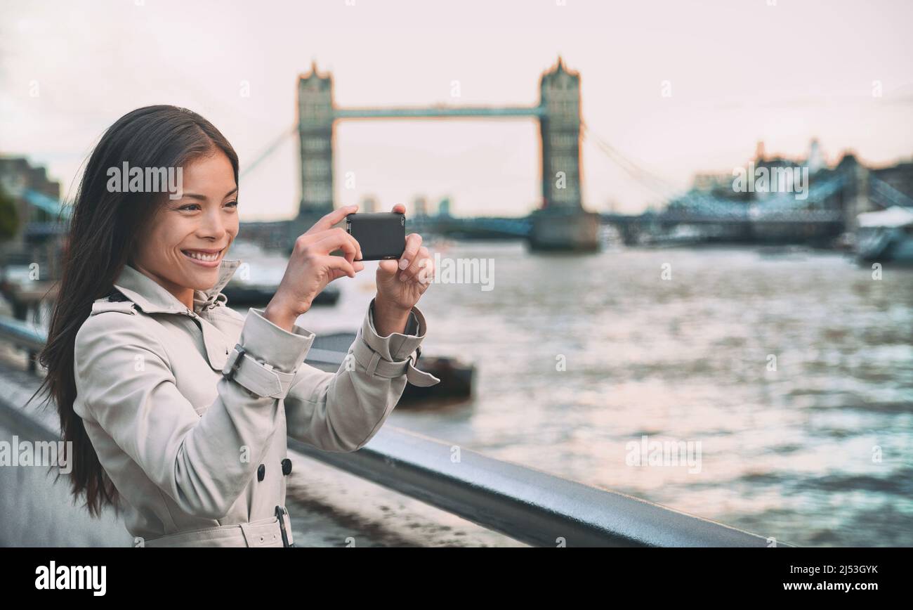 London woman tourist taking photo of Tower Bridge. London woman taking photos with mobile smart phone camera. Girl enjoying view over the River Thames Stock Photo