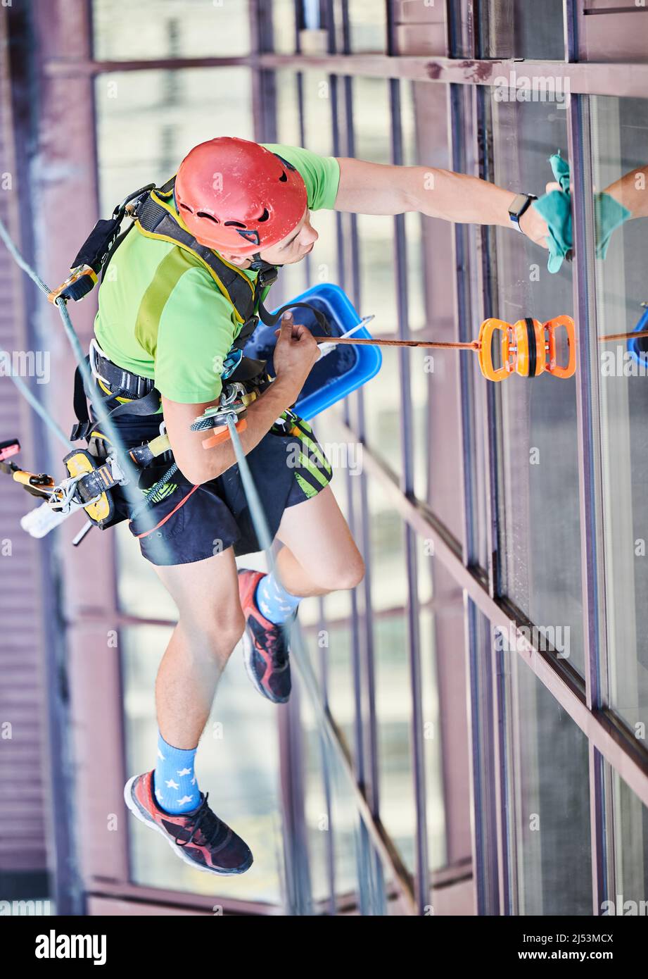Industrial mountaineering worker washing glass windows of high-rise ...