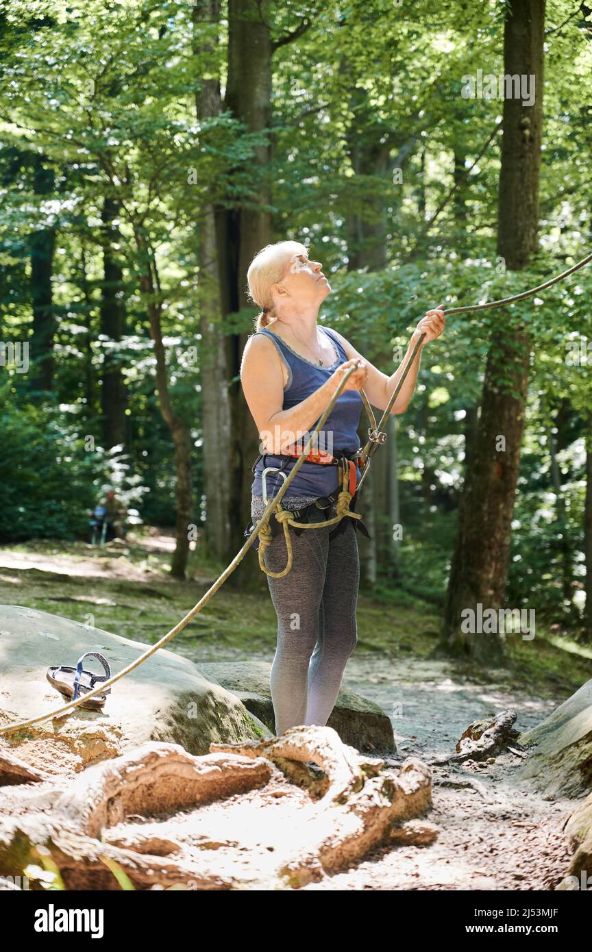 Female climber belaying leader during rock climbing outdoors, using rope and carabines. Elderly woman looking to his rope partner. Concept of teamwork, trust, extreme sport and outdoor activity. Stock Photo