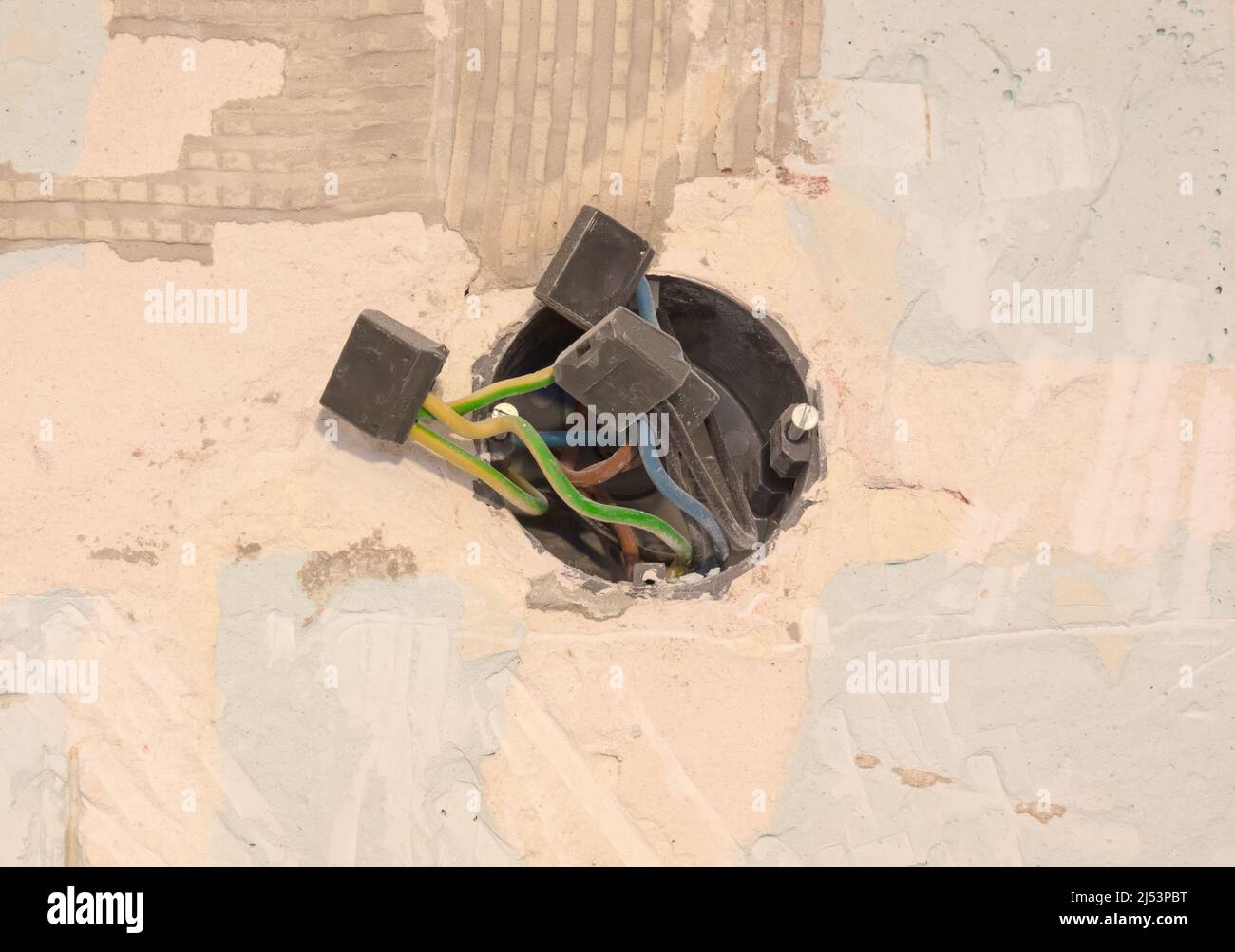 Risky open ends of electric wires hanging out from wall hole Stock