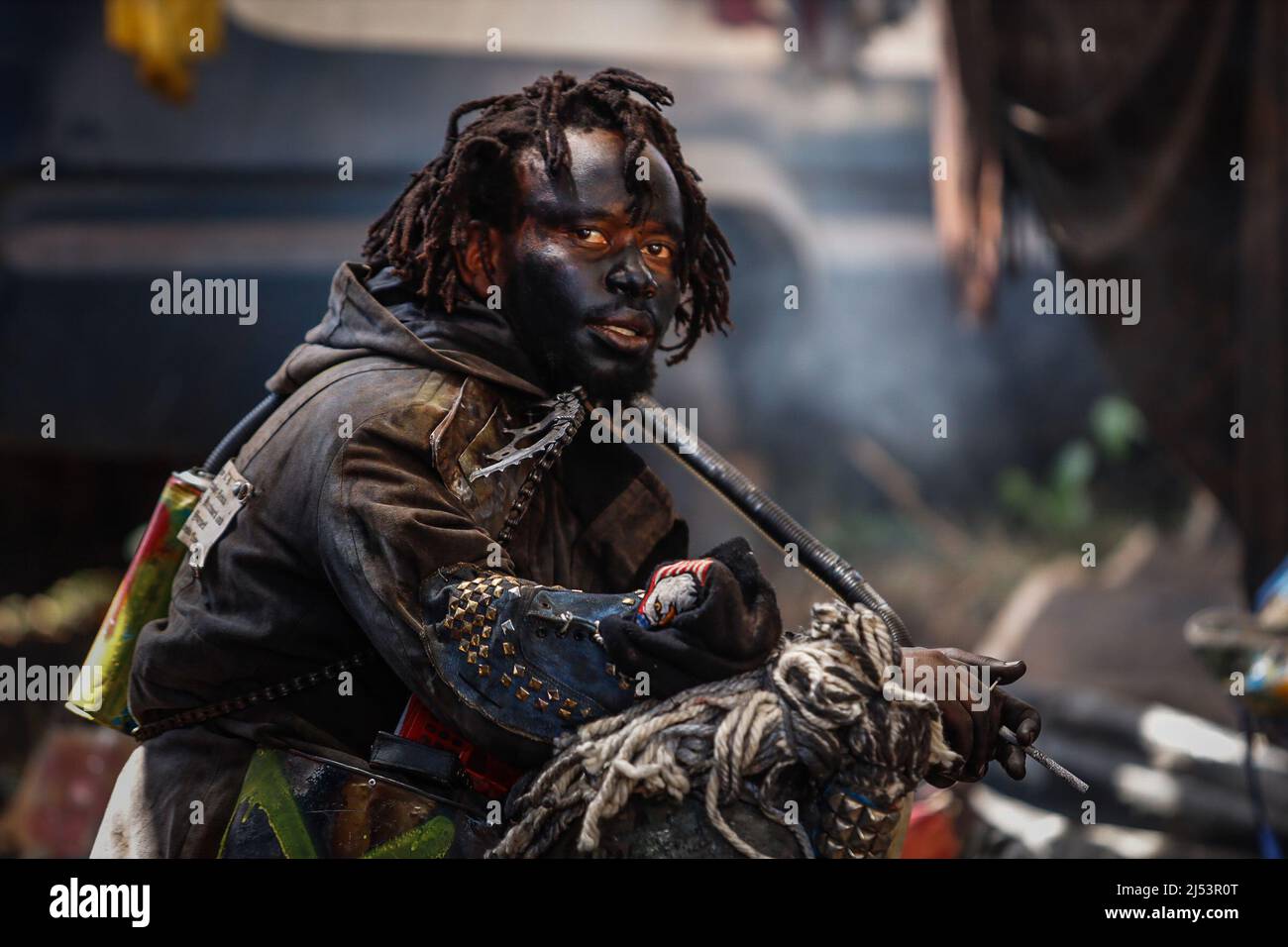 An artist dressed in a post-apocalyptic costume smokes a cigar during a  film production of a music video. Artists from Kibera dressed up in post-apocalyptic  costumes to shoot a music video focusing