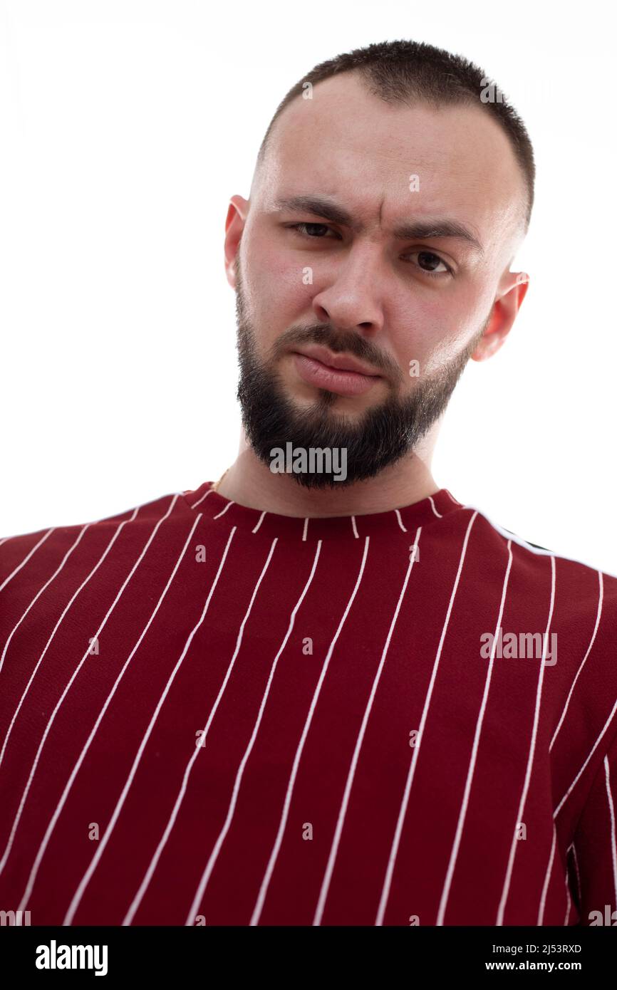 Portrait of young angry handsome bearded man with short dark hair wearing red striped sweatshirt, looking at camera Stock Photo