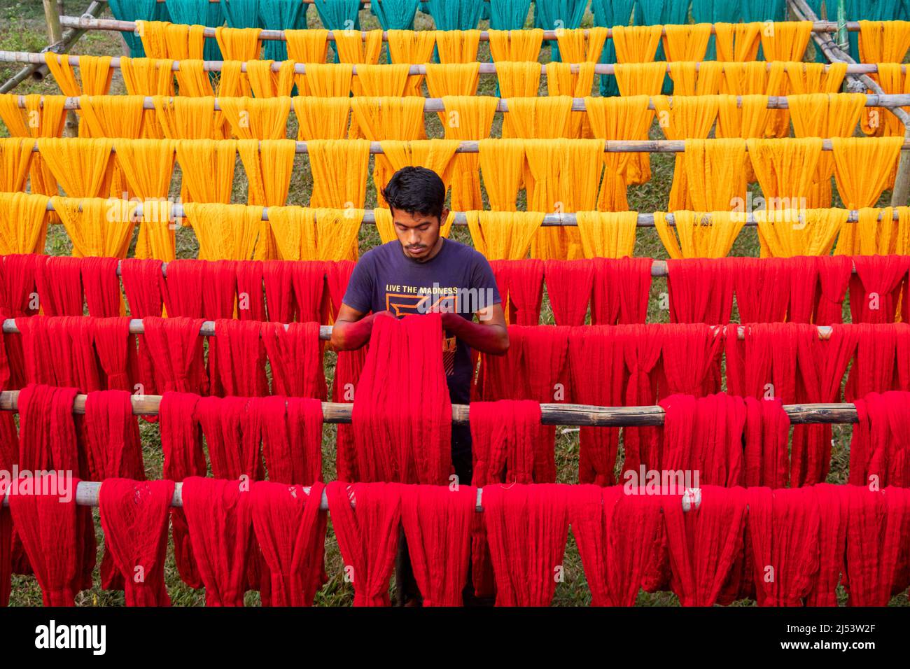 Narayanganj, Dhaka, Bangladesh. 20th Apr, 2022. A worker hangs thousands of freshly dyed colorful threads on a wooden structure as they are being dried in the sunshine in Narayanganj, Bangladesh. Thousands of colorful threads create a palette of colors as workers hang them out to dry. The threads take a whole day to dry and stretch for hundreds of meters. Once dried, they are sold to wholesale markets. Each row of threads is priced for Â£2. The workers spend 12 hours in the fields during this process, earning Â£5 per day. (Credit Image: © Joy Saha/ZUMA Press Wire) Stock Photo