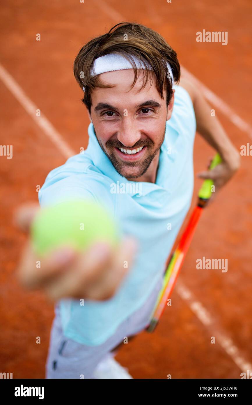 Young handsome tennis player with racket and ball prepares to serve at ...