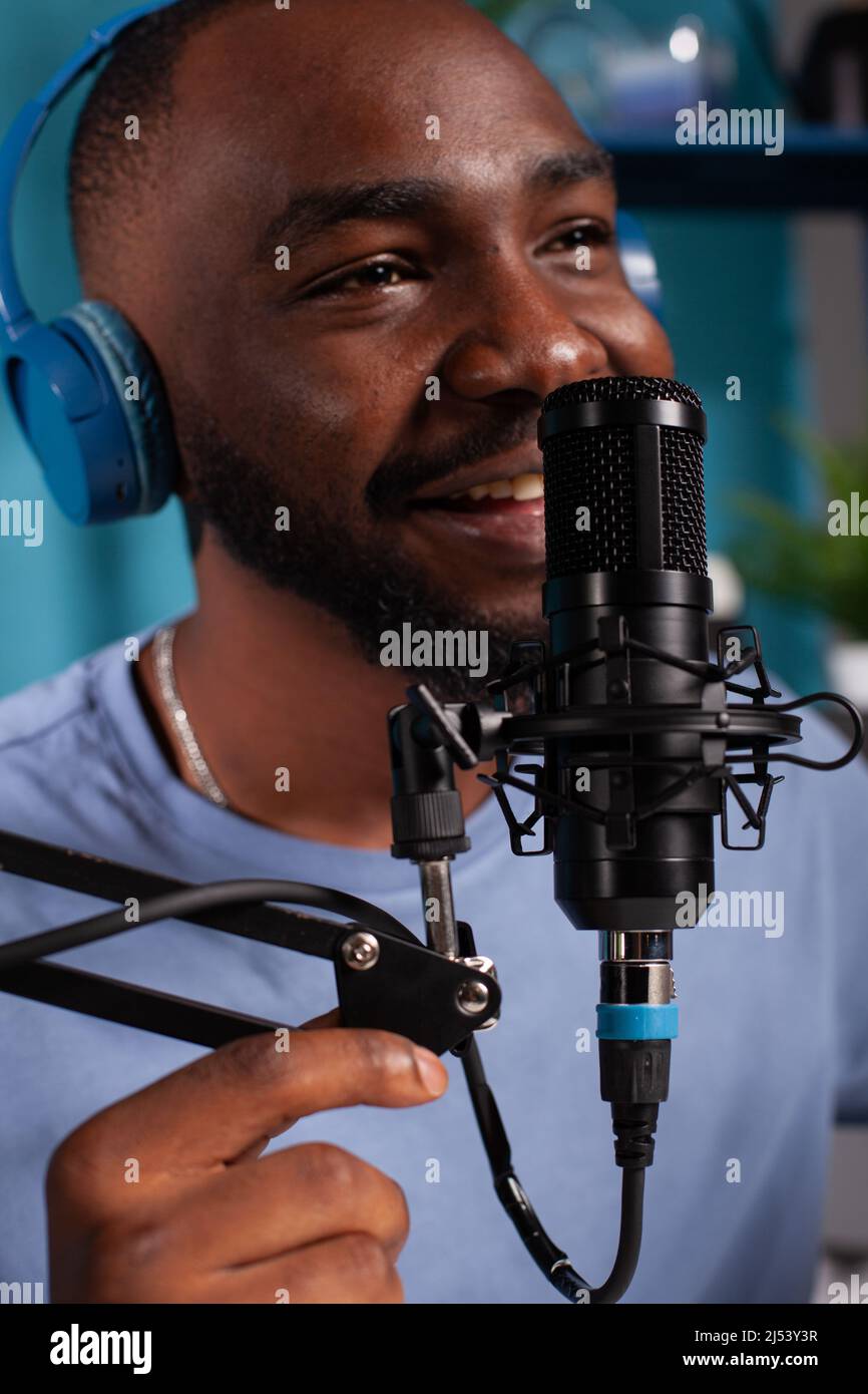Closeup of smiling vlogger talking to audience using professional microphone wearing wireless headphones in live podcast. Close focus on studio mic used by content creator in online interview. Stock Photo