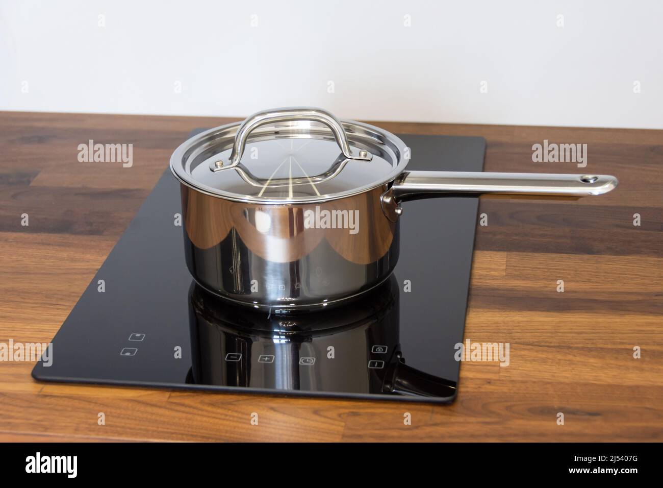 Saucepan ladle with lid on an induction hob built into a wooden kitchen