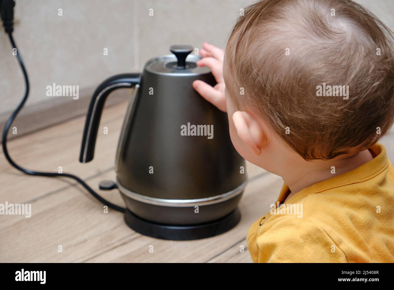 Toddler baby boy holds a hot kettle with boiling water. Child safety