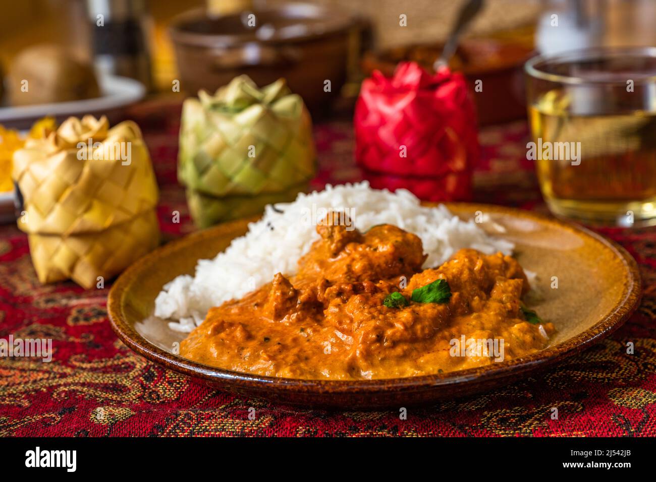 Indian chicken tikka masala with rice on plate, 3 bamboo spice box, cup of tea, fruit on red table-cloth on table, closeup. Stock Photo