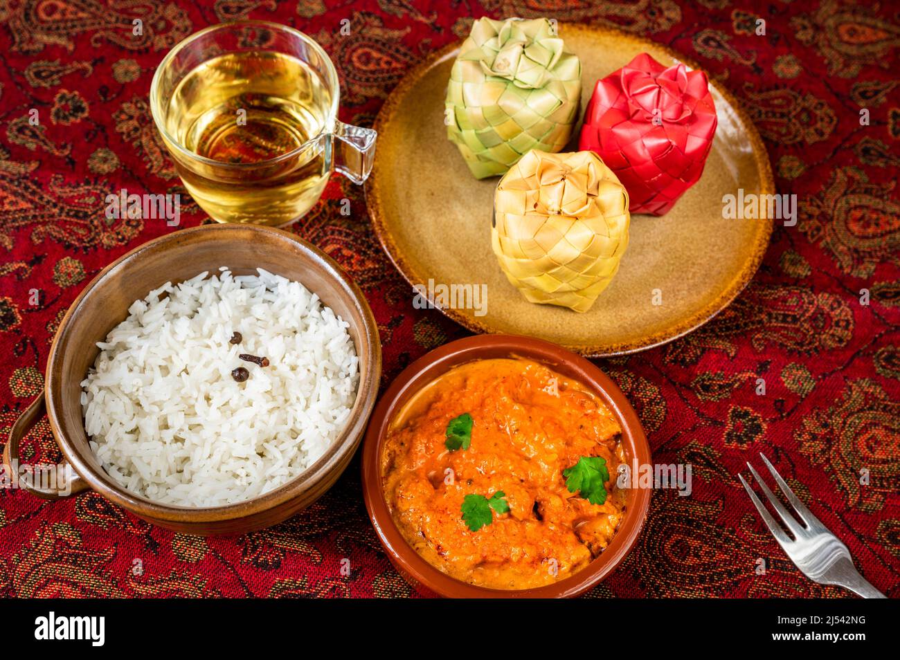 Chicken tikka masala, stewed rice, cup of tea, 3 bamboo spice container on plate on red oriental table-cloth. Indian meal. Stock Photo