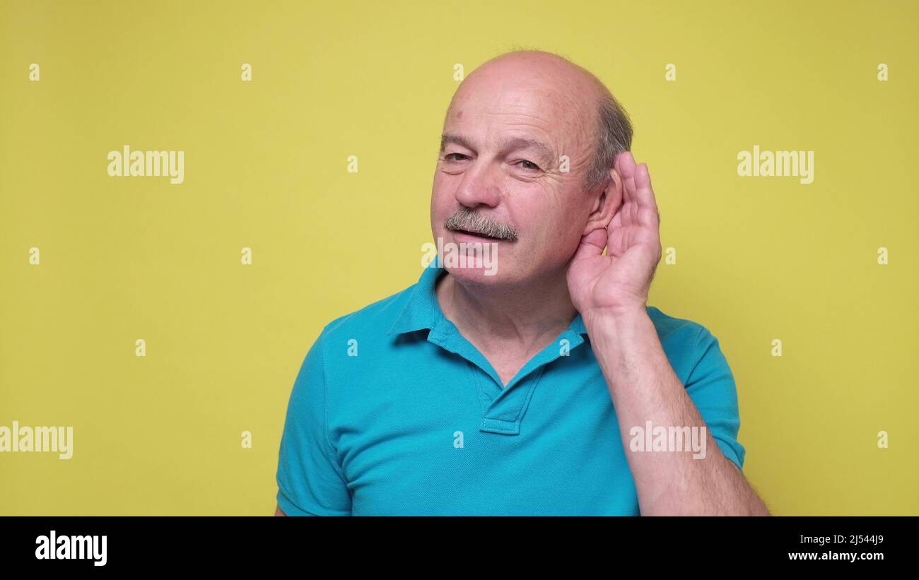 Senior man trying to listen to the latest news holding hand near ear. Studio shot Stock Photo Alamy