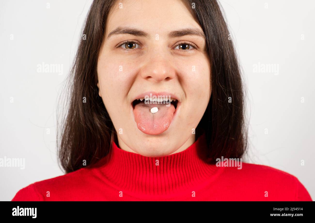 A woman takes a pill, a white round pill on the tongue in a person's mouth Stock Photo