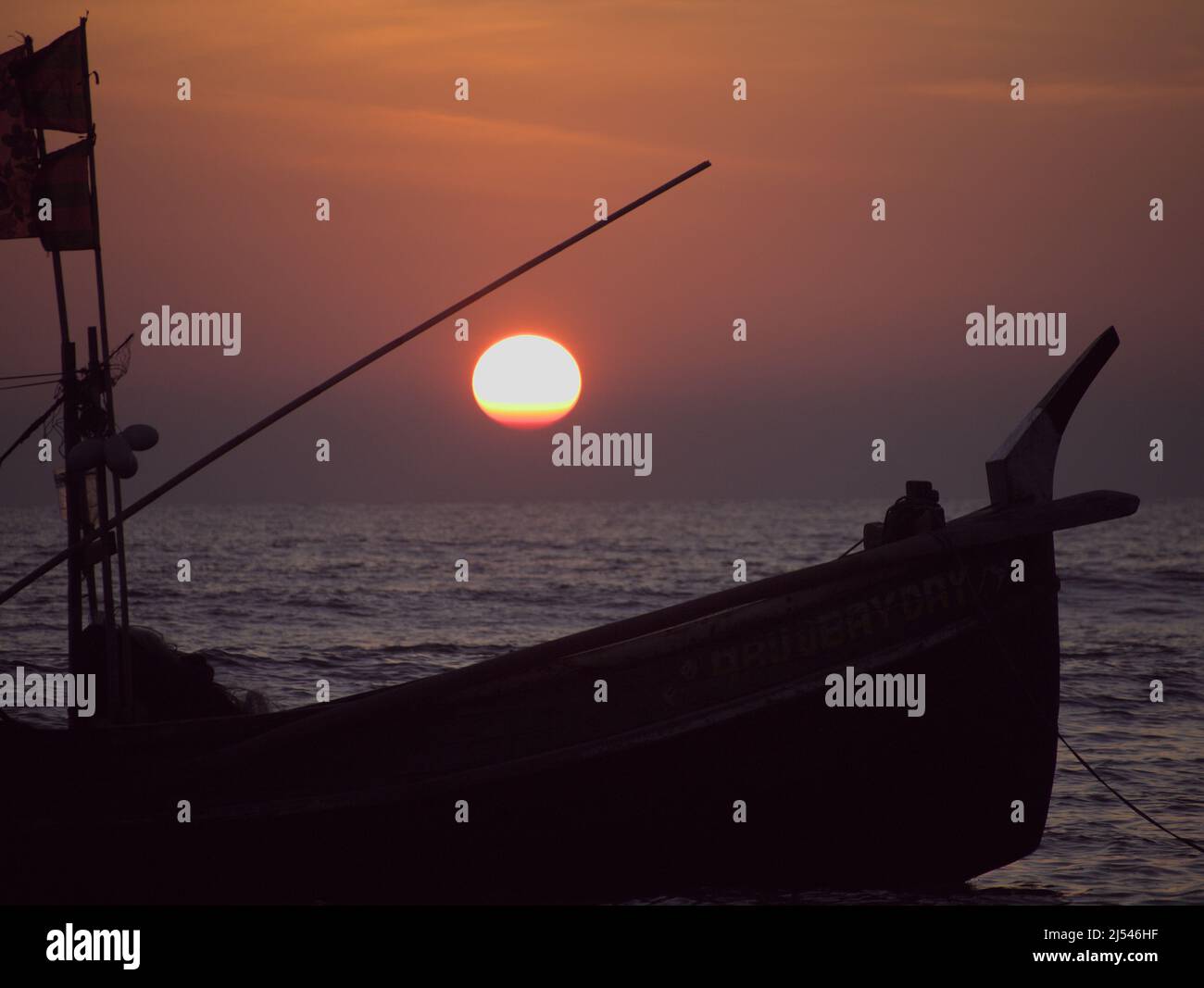 The sun sets behind the silhoutte of a local Balami Nouka fishing boat off Cox's Bazar beach, Bangladesh Stock Photo