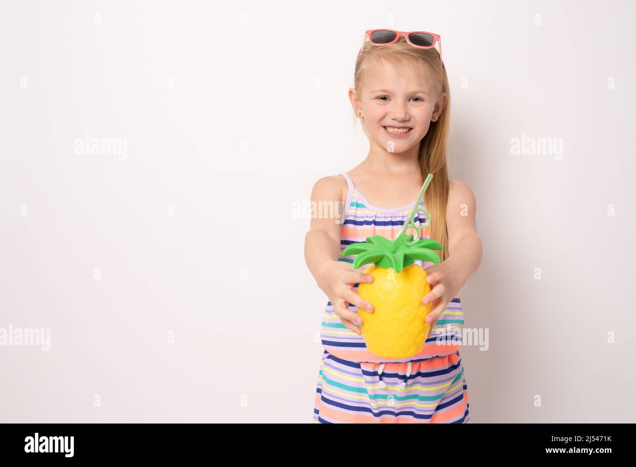 Portrait of happy little girl in summer clothing drinking orange juice ...