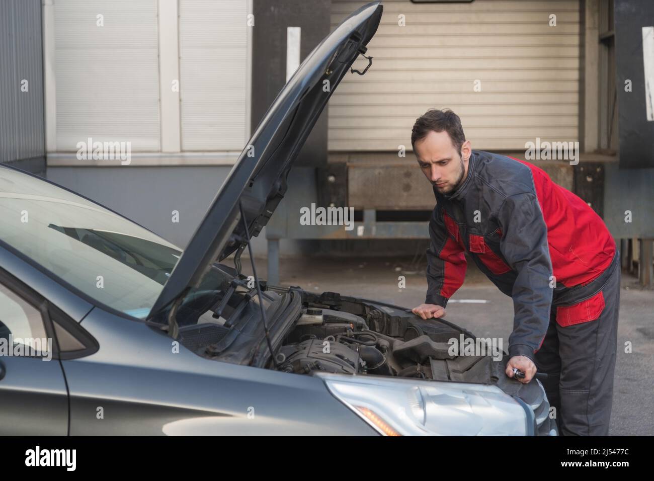 Auto mechanic examines condition of the car under the hood at car diagnostics station. Stock Photo