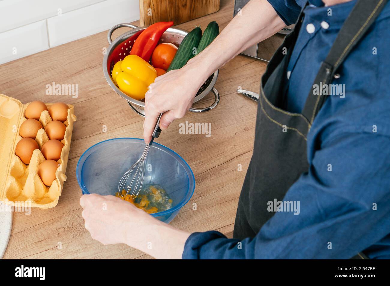 https://c8.alamy.com/comp/2J547BE/top-view-of-unrecognizable-man-in-blue-long-sleeve-shirt-beating-eggs-in-blue-plastic-bowl-with-wire-whisk-on-table-near-steel-colander-with-red-yell-2J547BE.jpg
