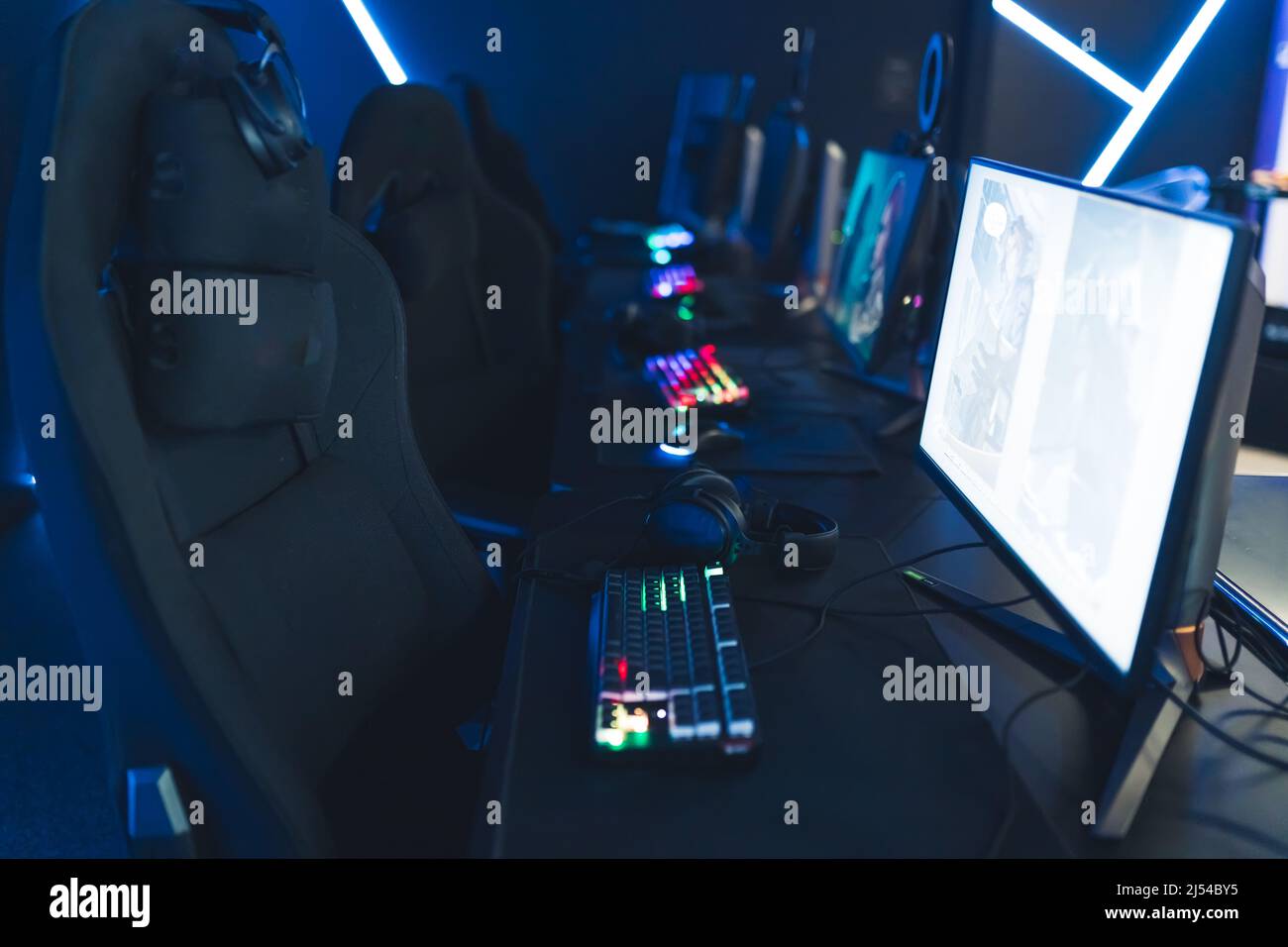 Empty glow neon illuminated cybercafe room with computers on tables, professional seats, and illuminated keyboards no people. Modern cyber sport. High quality photo Stock Photo