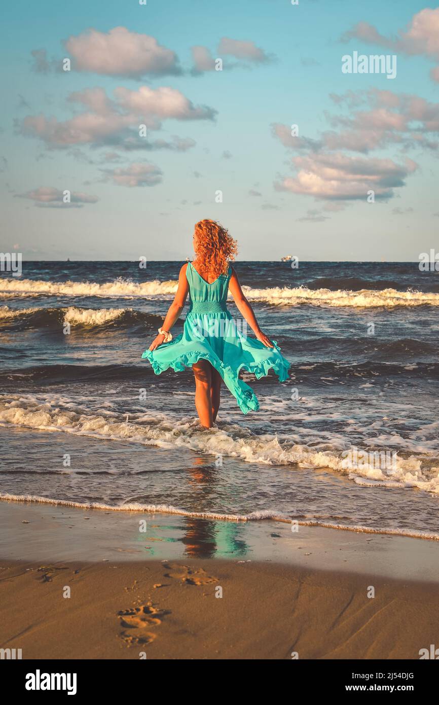 Beautiful blonde haired woman on the beach. Girl in a blue dress at the Polish seaside. Stock Photo