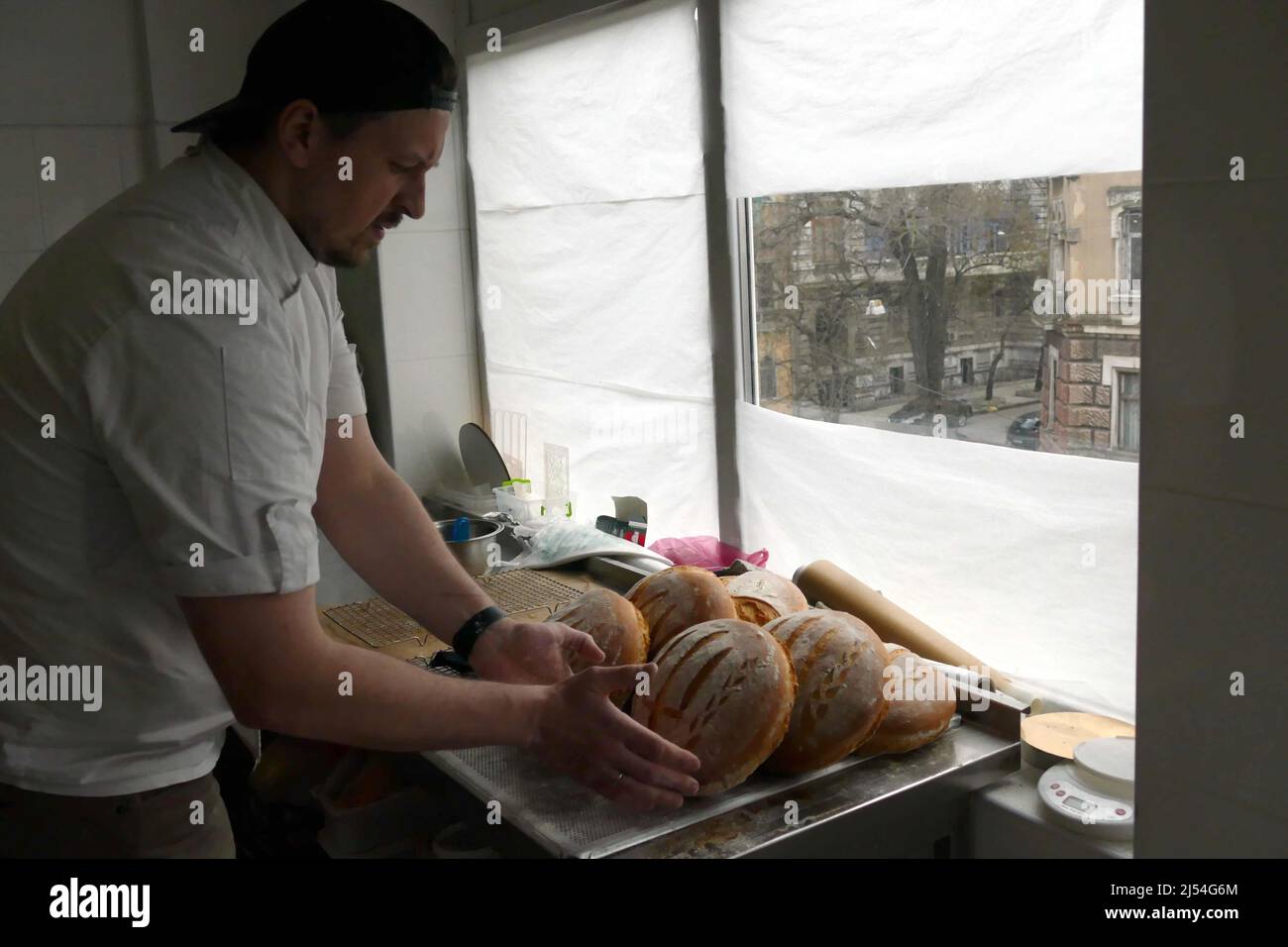ODESA, UKRAINE - APRIL 18, 2022 - Baker Oleksii Babenko arranges bread loaves on a tray at a local bakery that makes bread decorated with the tryzub, Stock Photo