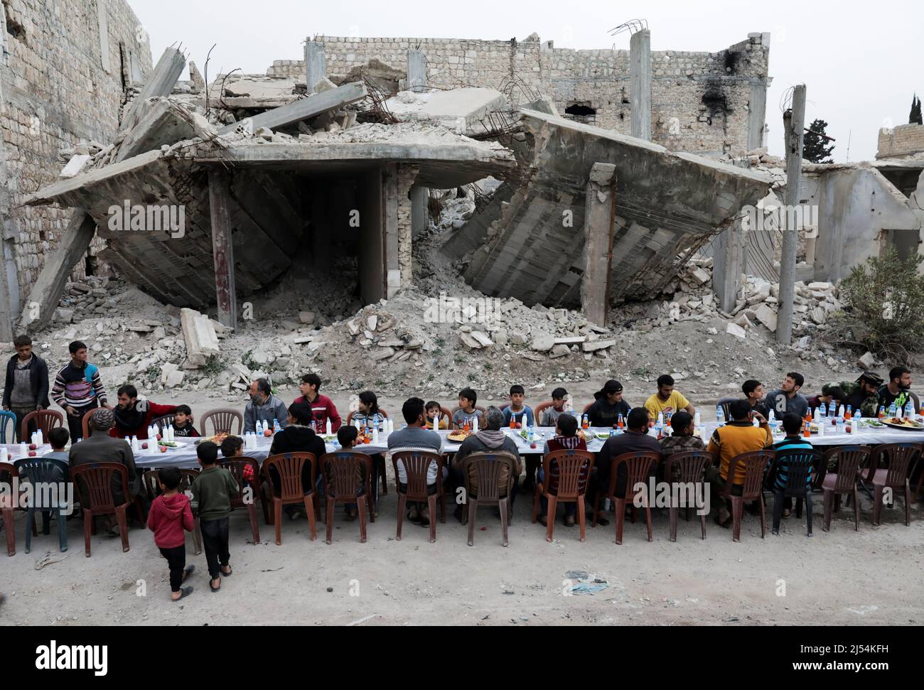 People gather amidst damaged buildings during Iftar (breaking fast), during the holy month of Ramadan, in the town of Tadef, on a frontline between Russian-backed Syrian government forces and Turkish-backed Syrian rebel-held territory, in northern Syria April 18, 2022. Picture taken April 18, 2022.  REUTERS/Khalil Ashawi Stock Photo