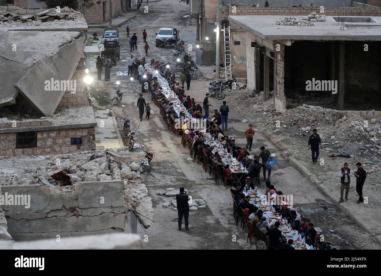 People gather amidst damaged buildings during Iftar (breaking fast), during the holy month of Ramadan, in the town of Tadef, on a frontline between Russian-backed Syrian government forces and Turkish-backed Syrian rebel-held territory, in northern Syria April 18, 2022. Picture taken April 18, 2022.  REUTERS/Khalil Ashawi Stock Photo
