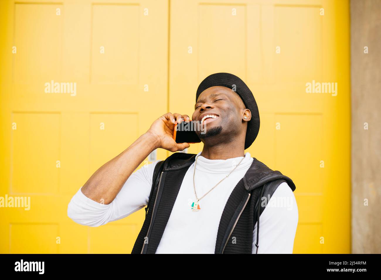Portrait of a young smiling black male talking on a phone against a yellow door Stock Photo