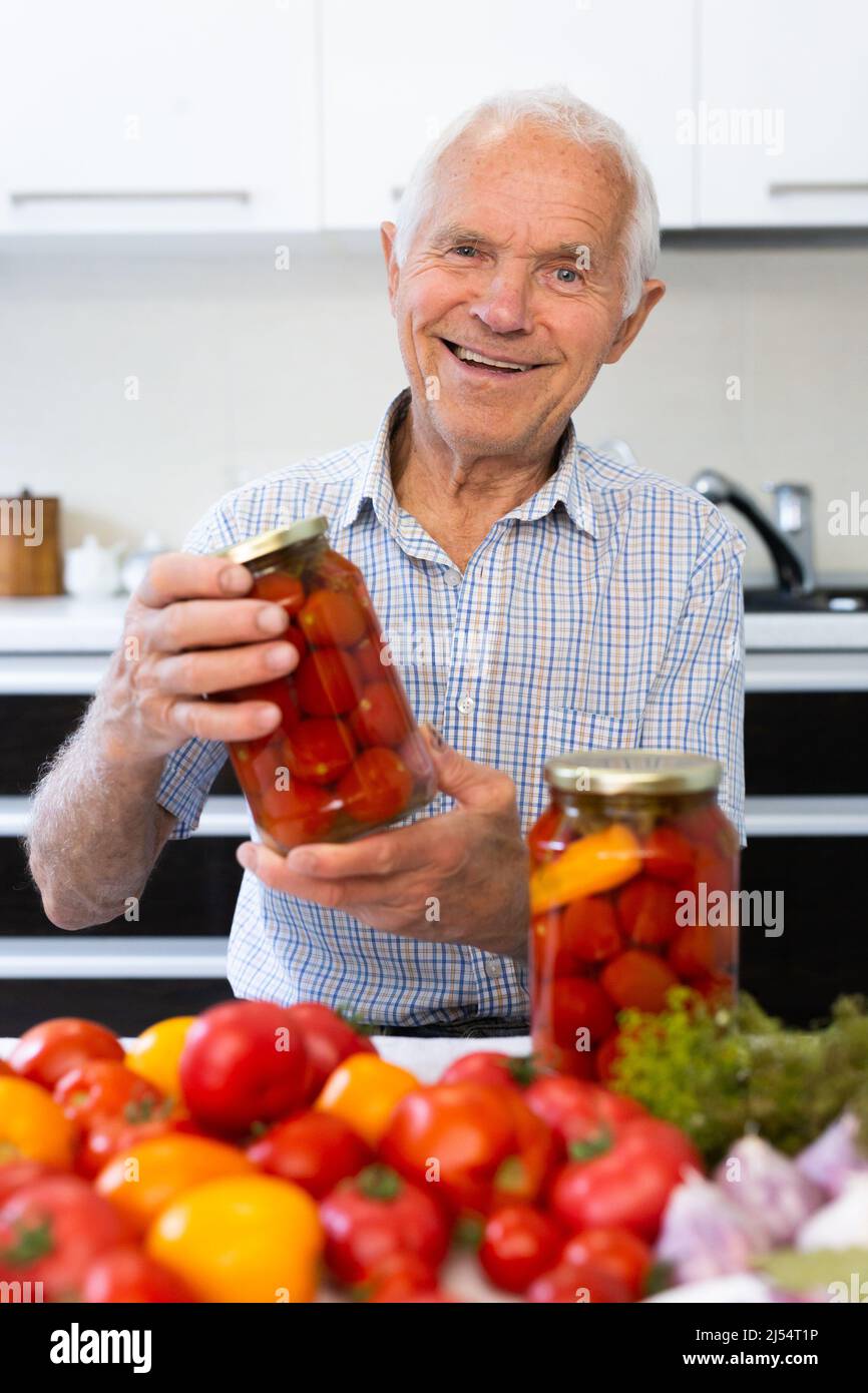 old man holding jars of pickled tomatoes and smiling Stock Photo