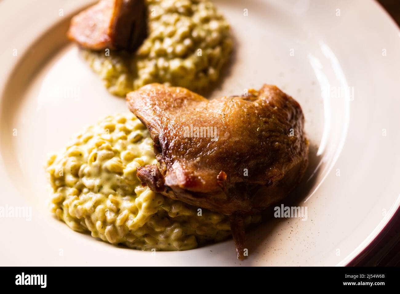 dish duck leg with green perlotto served on a white plate Stock Photo