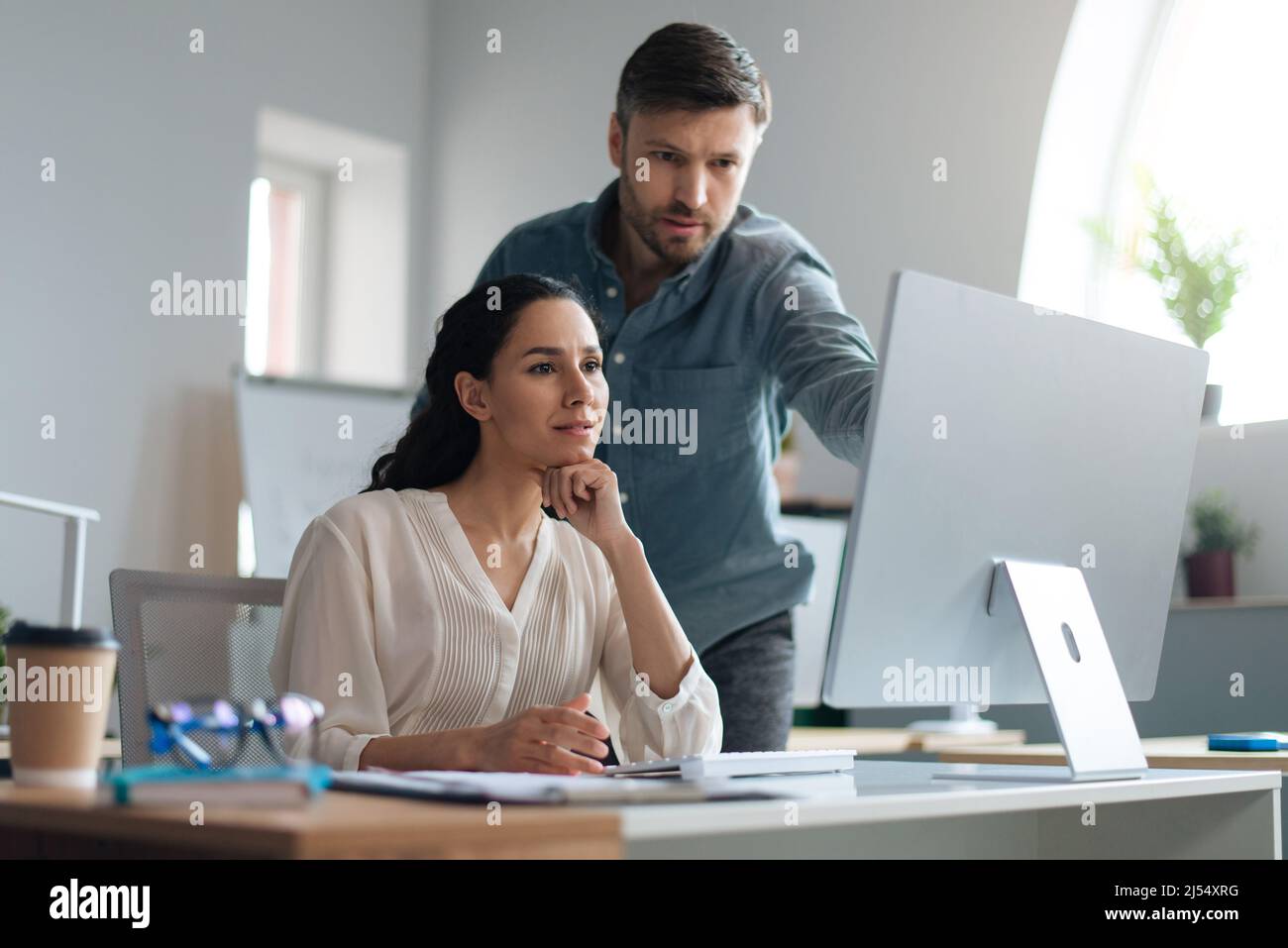 Young female trainee working on computer together with her business mentor at modern company office Stock Photo