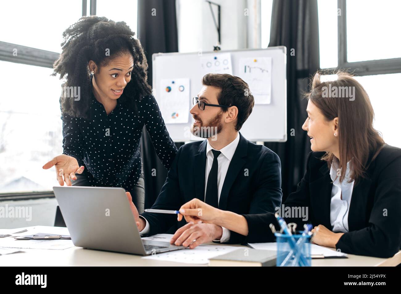 Team collaboration. Business partners working together on a project. Multiracial colleagues are brainstorming on strategy together, sitting in modern office, studying documents,using laptop,discussing Stock Photo