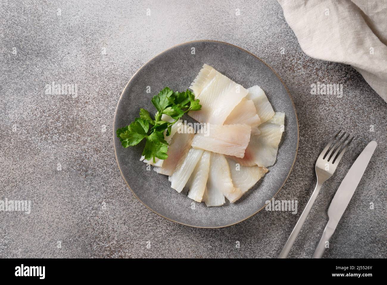 Delicious smoked halibut slices served with parsley on gray background. View from above. Copy space. Stock Photo