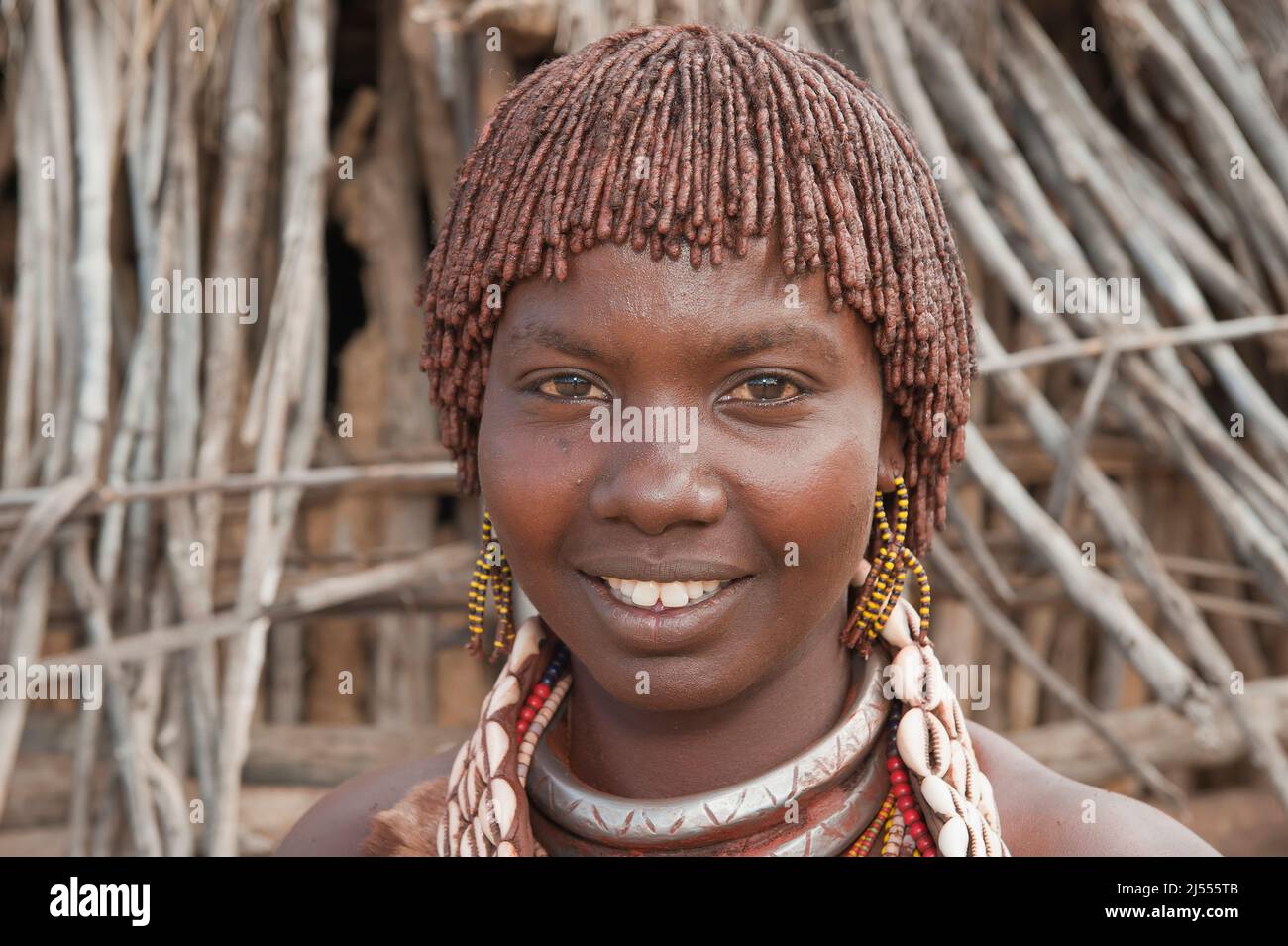 Young Hamar woman with red clay in her hair and necklaces made of Cowry