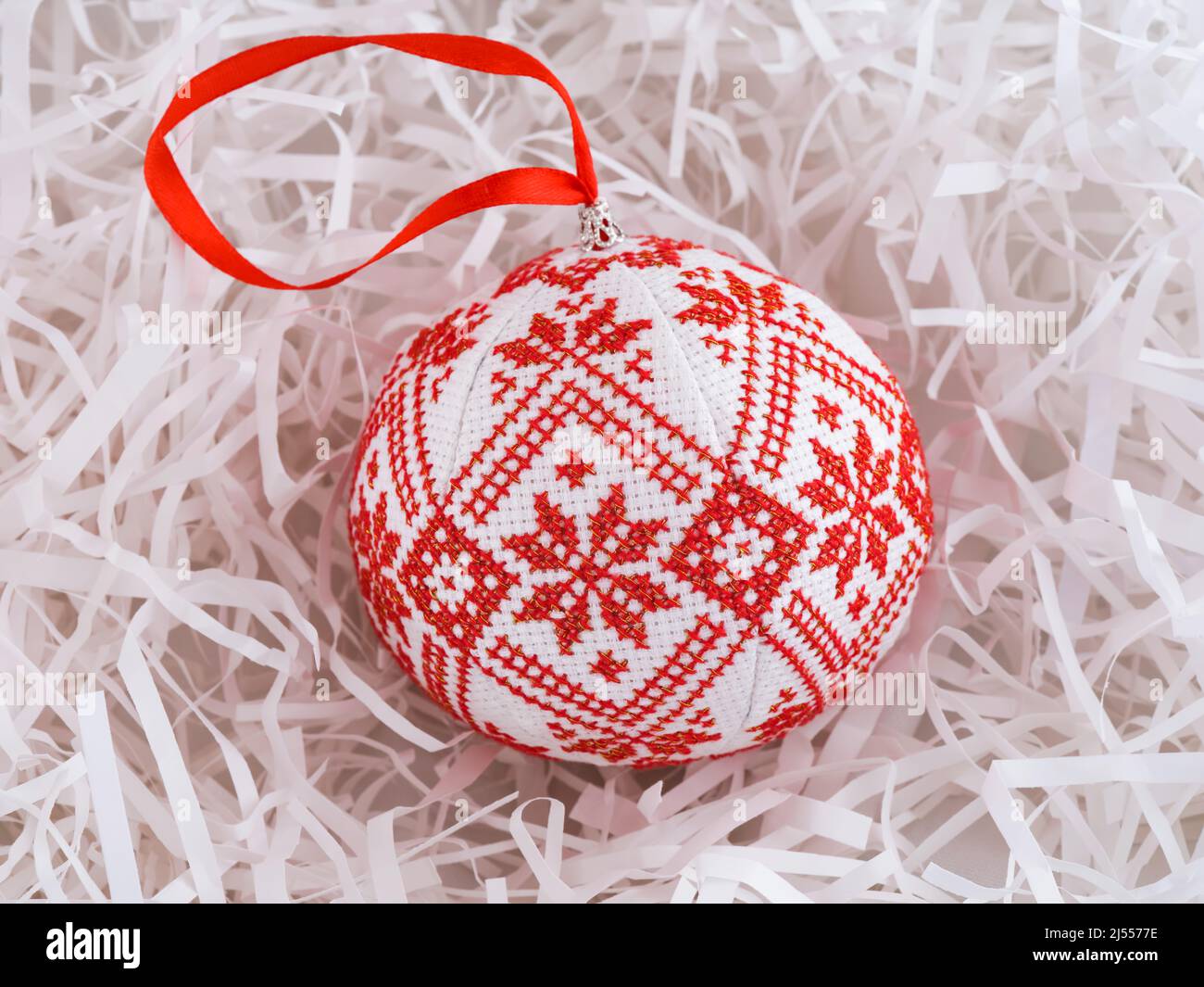 Cross stitched christmas ornament on white shredded wrapping paper background. Christmas ornament made by me. Stock Photo