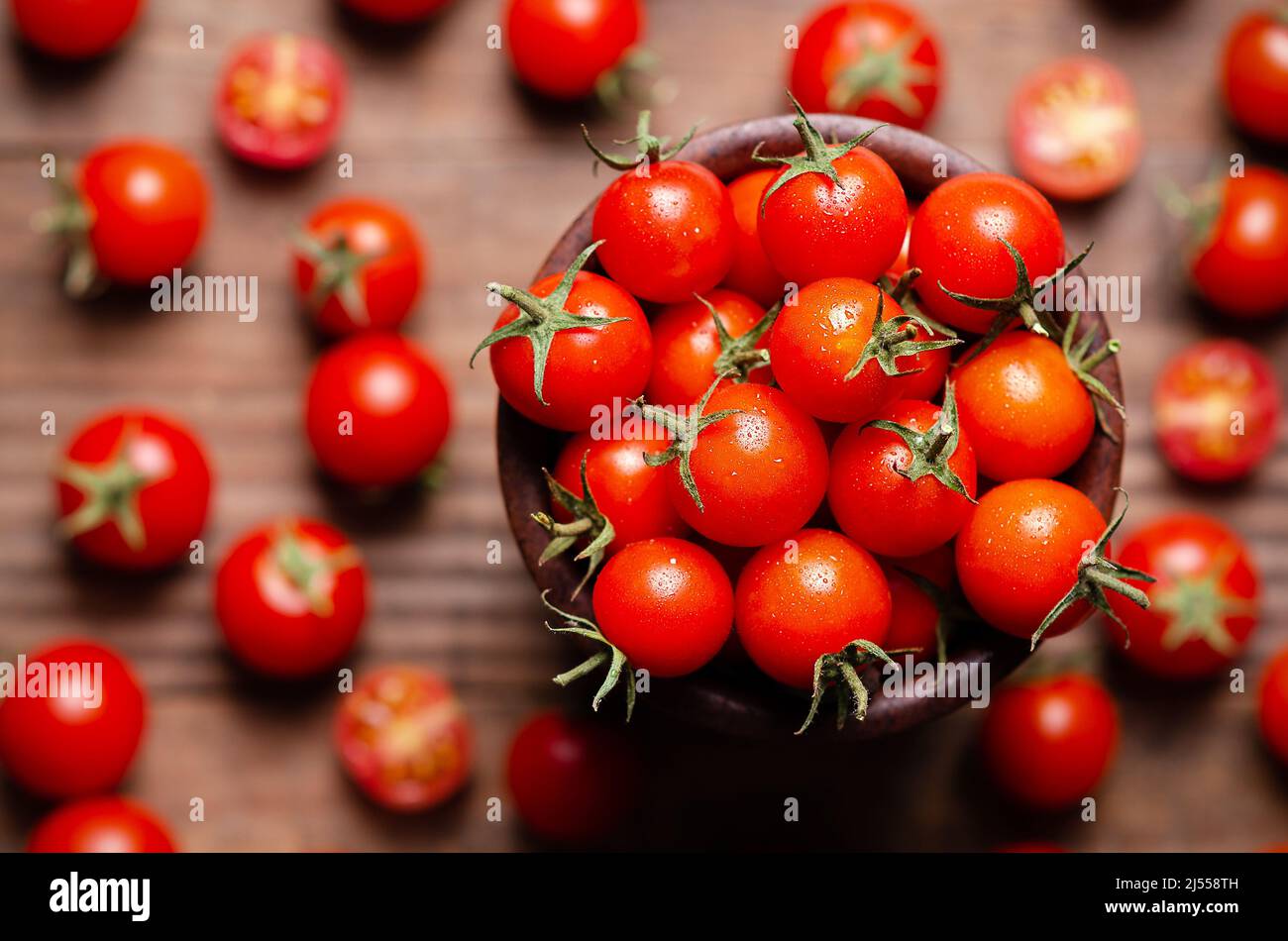 Red cherry tomatoes in a wooden bowl on a wooden background. Top view ...