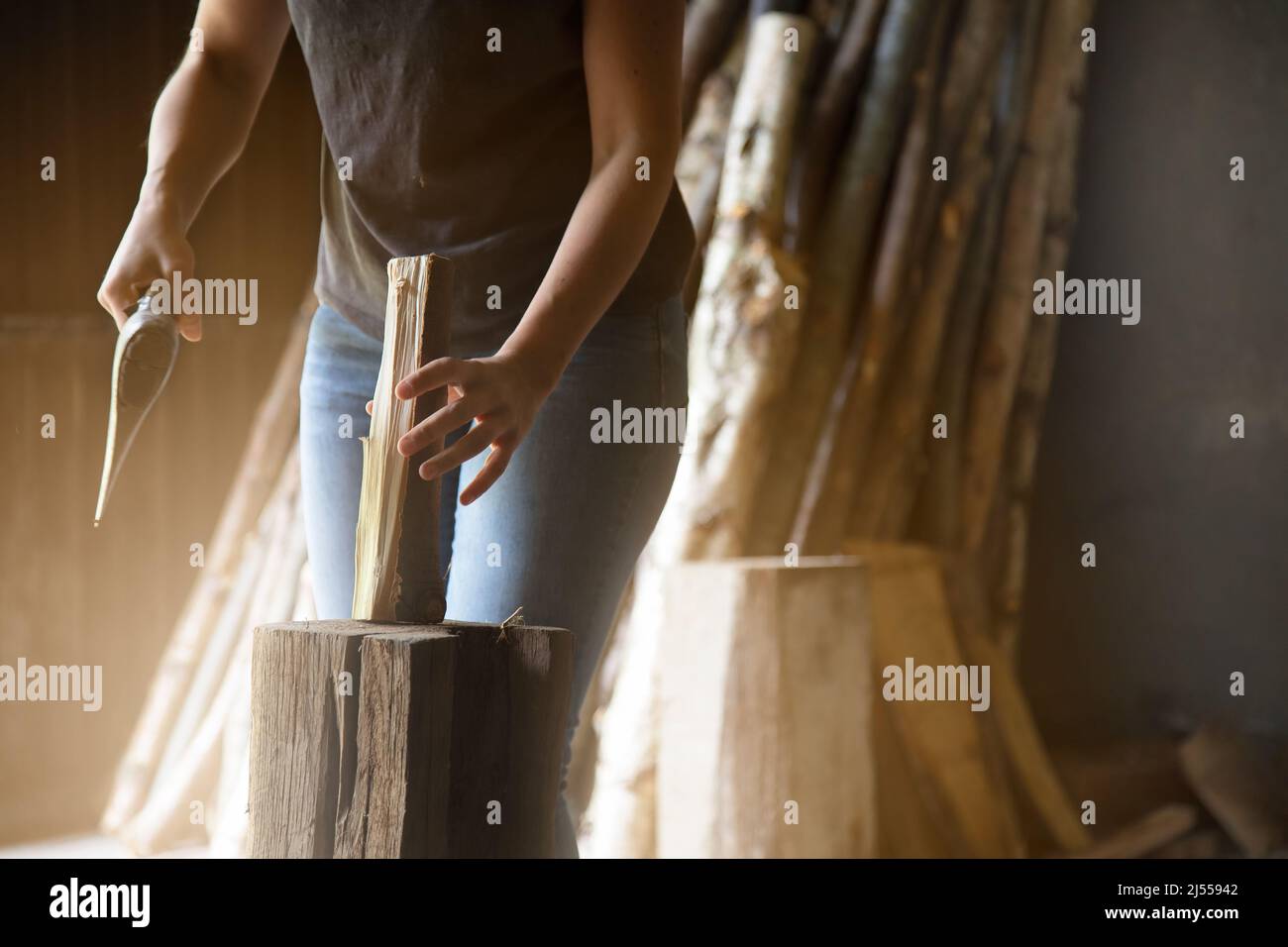 close-up of an unrecognizable woman holding a piece of wood to split it into smaller pieces to make firewood. logs in the background Stock Photo