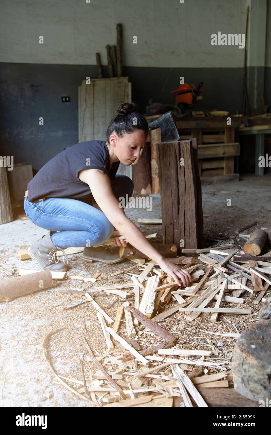 vertical photo of a girl collecting firewood from the ground that she has cut with an hatchet . men's work done by a woman. empowerment. Copy space Stock Photo