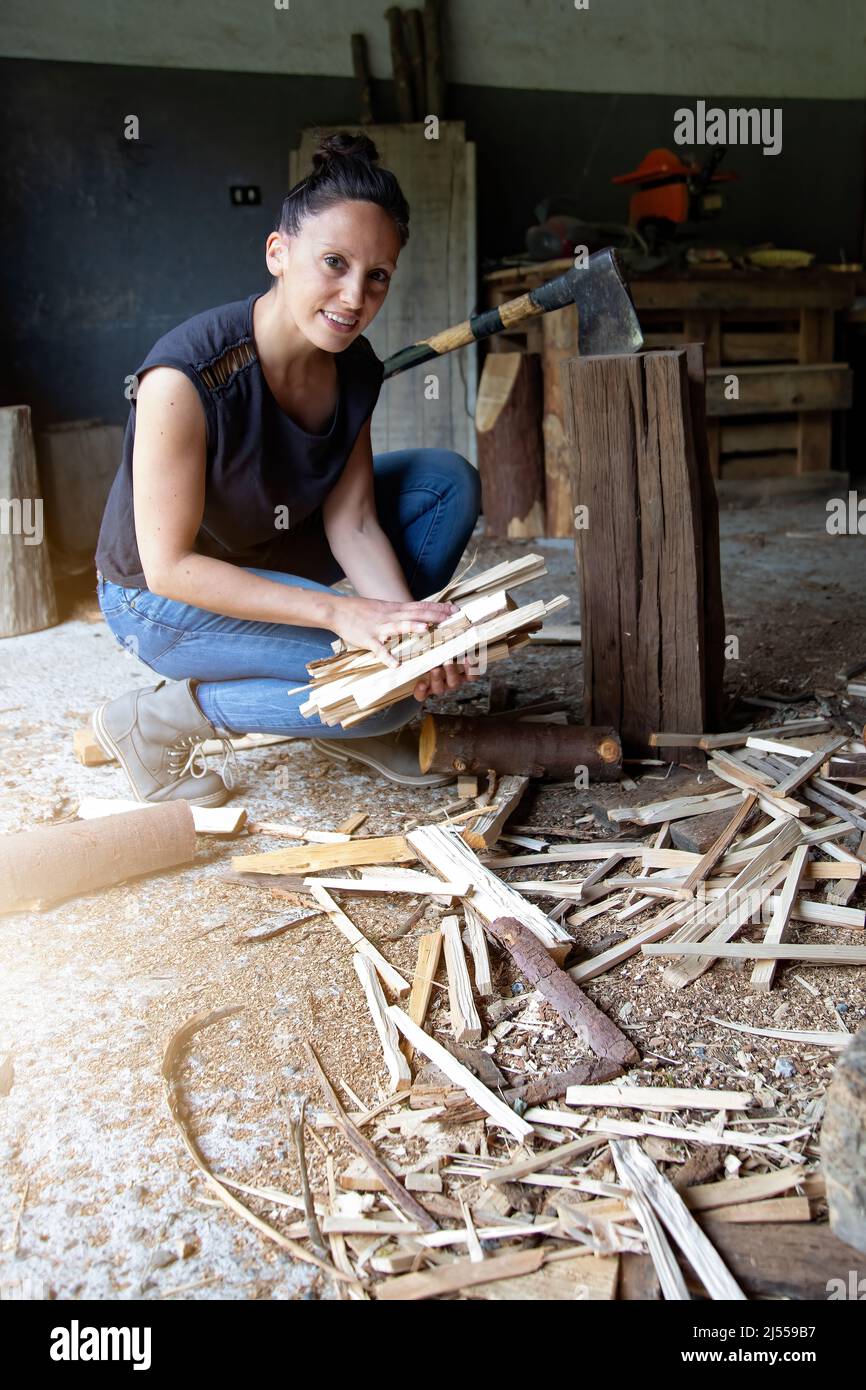 vertical photograph of a smiling woman crouching on the ground gathering freshly cut firewood to make a fire. equality at work. empowerment. strength. Stock Photo