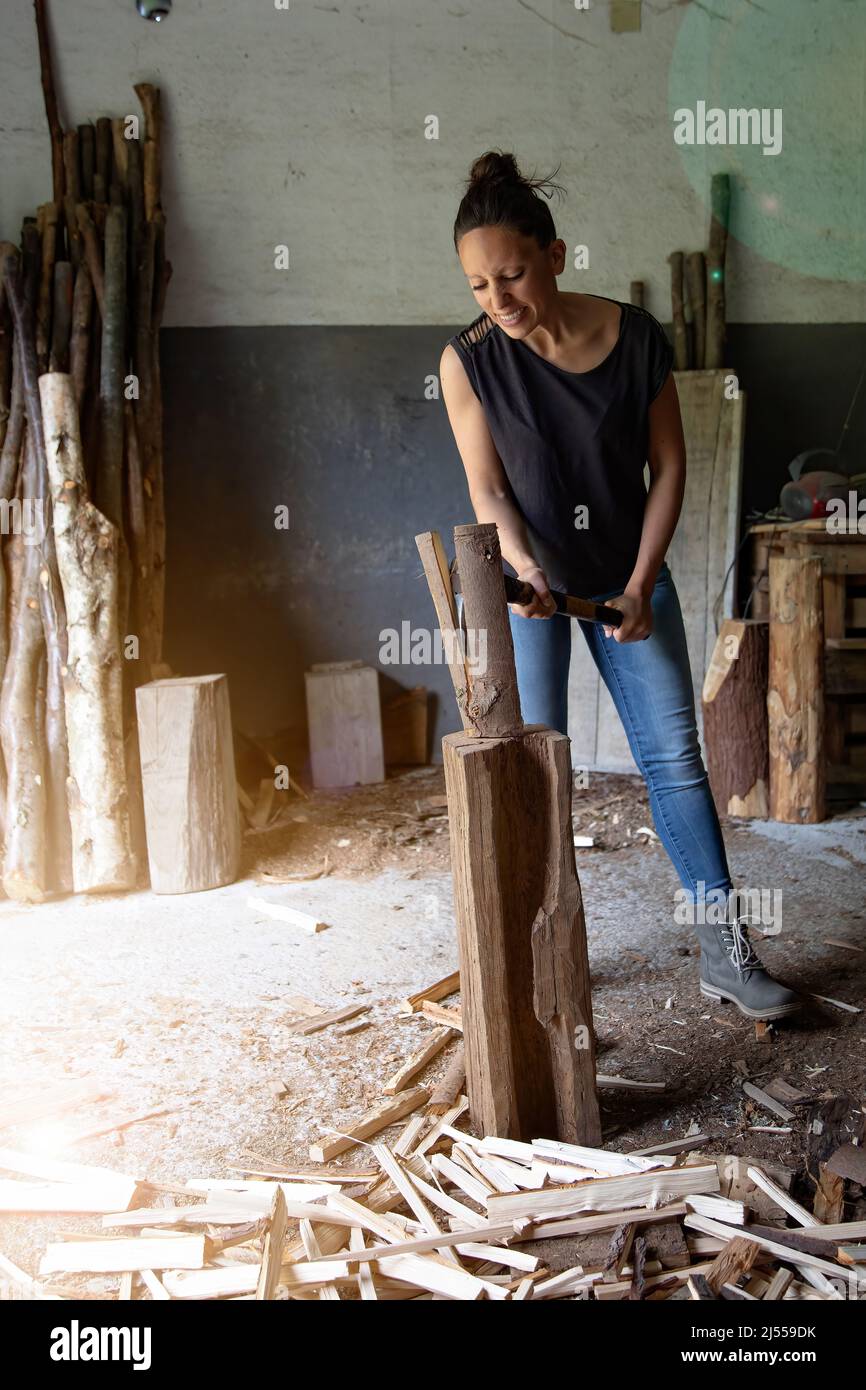vertical photograph of a young woman chopping wood to make fire with a smile on her face. female empowerment. equality in the workplace. Copy space Stock Photo