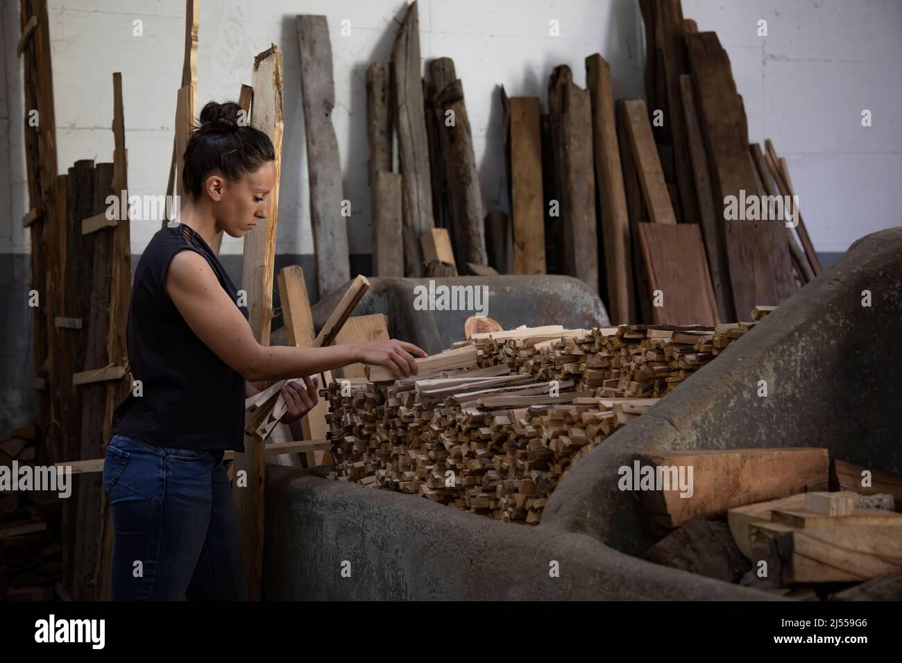 brunette woman with her hair in a bun working while repositioning freshly cut wood to light the fire in the storehouse. Copy space Stock Photo
