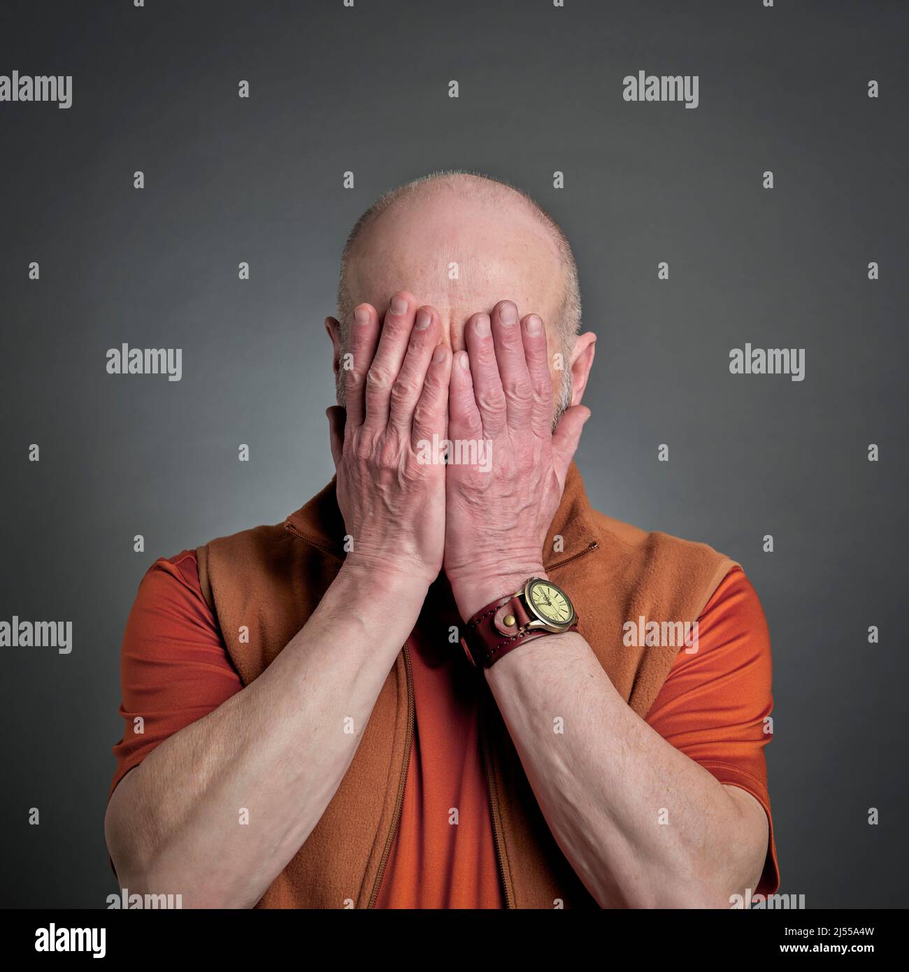 casual portrait of a senior bald man covering his face with hands ...