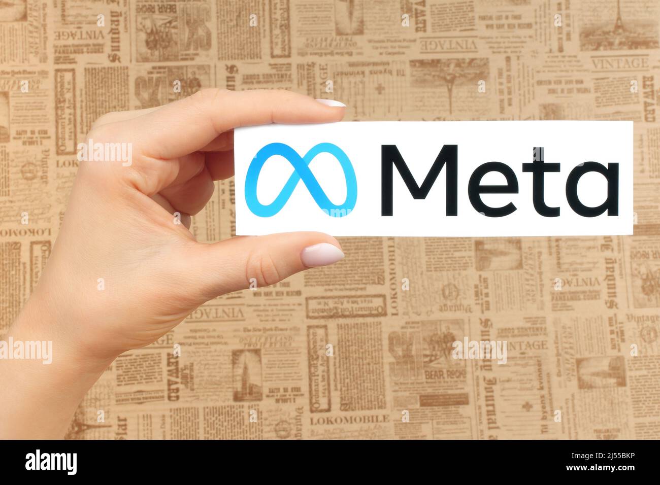 Kiev, Ukraine - January 20, 2022: Hand holds Meta logo, on old newspaper background. Social media giant Facebook is rebranding as Meta Stock Photo