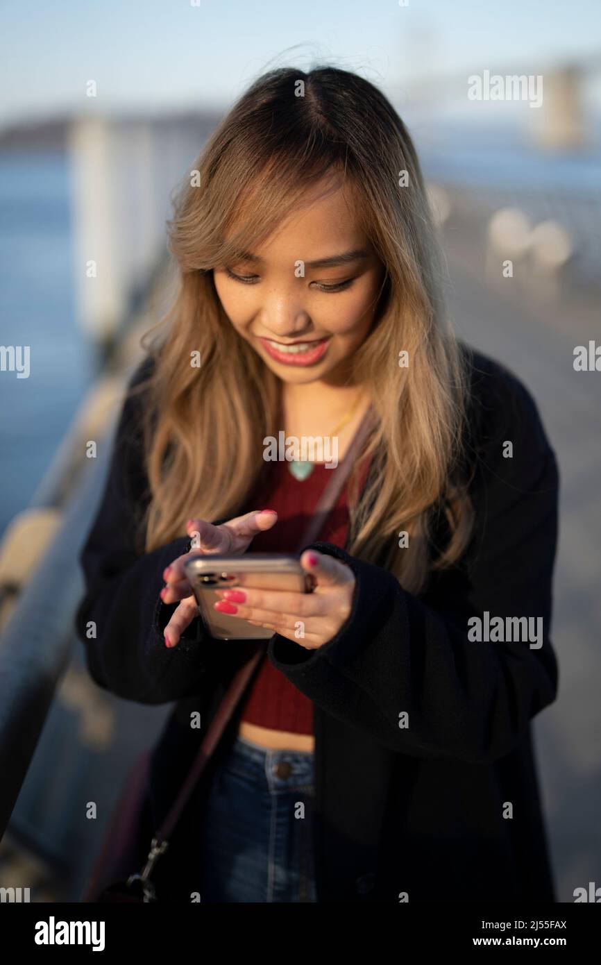 Beautiful Young Woman Looking for a Photograph Share on Her Smart Phone with SF Marina in the Background | Social Media Smartphone Stock Photo