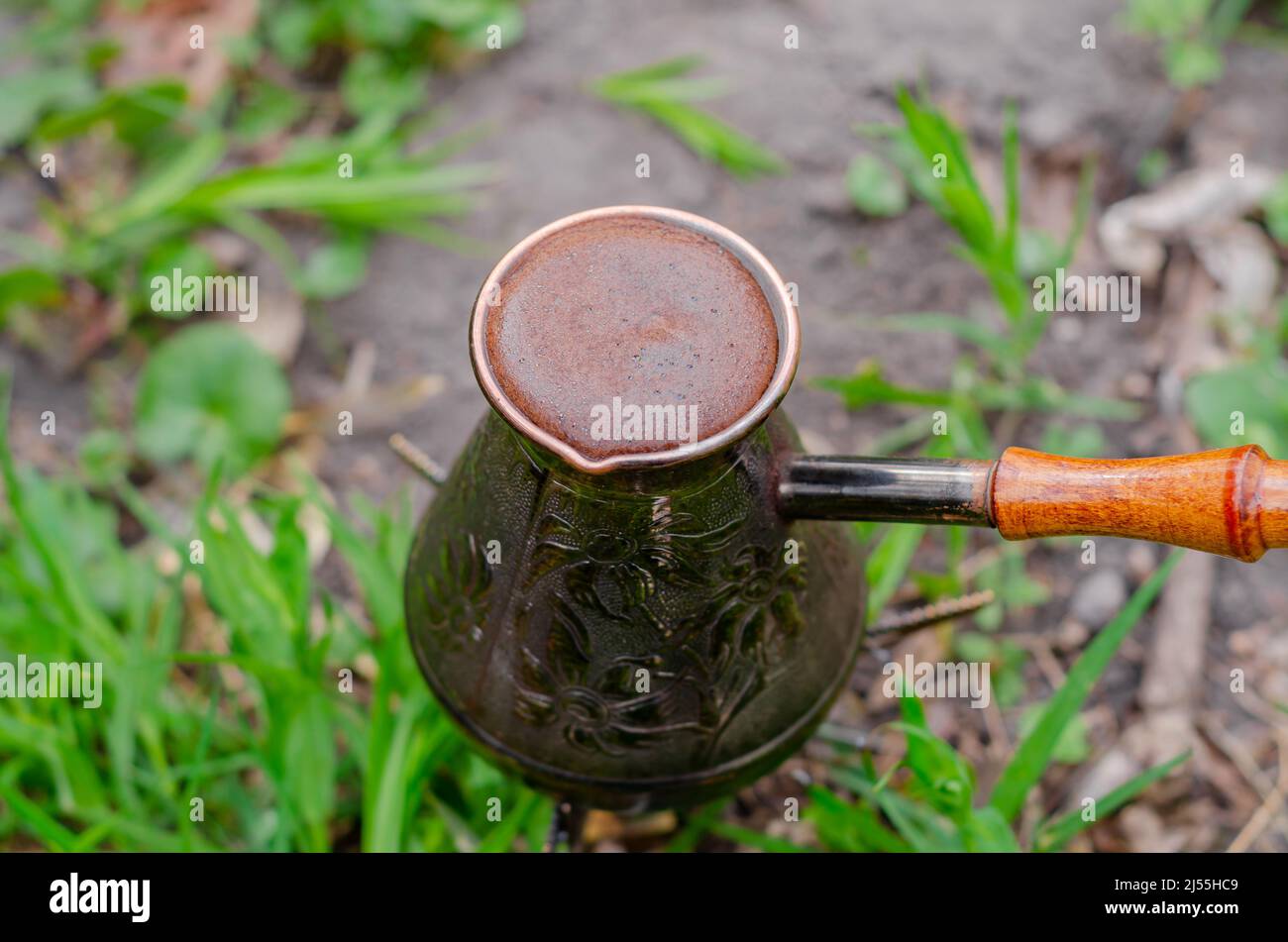 Aromatic delicious coffee in copper patterned turk with wooden handle. Coffee in the woods on grass. Top view close up Stock Photo