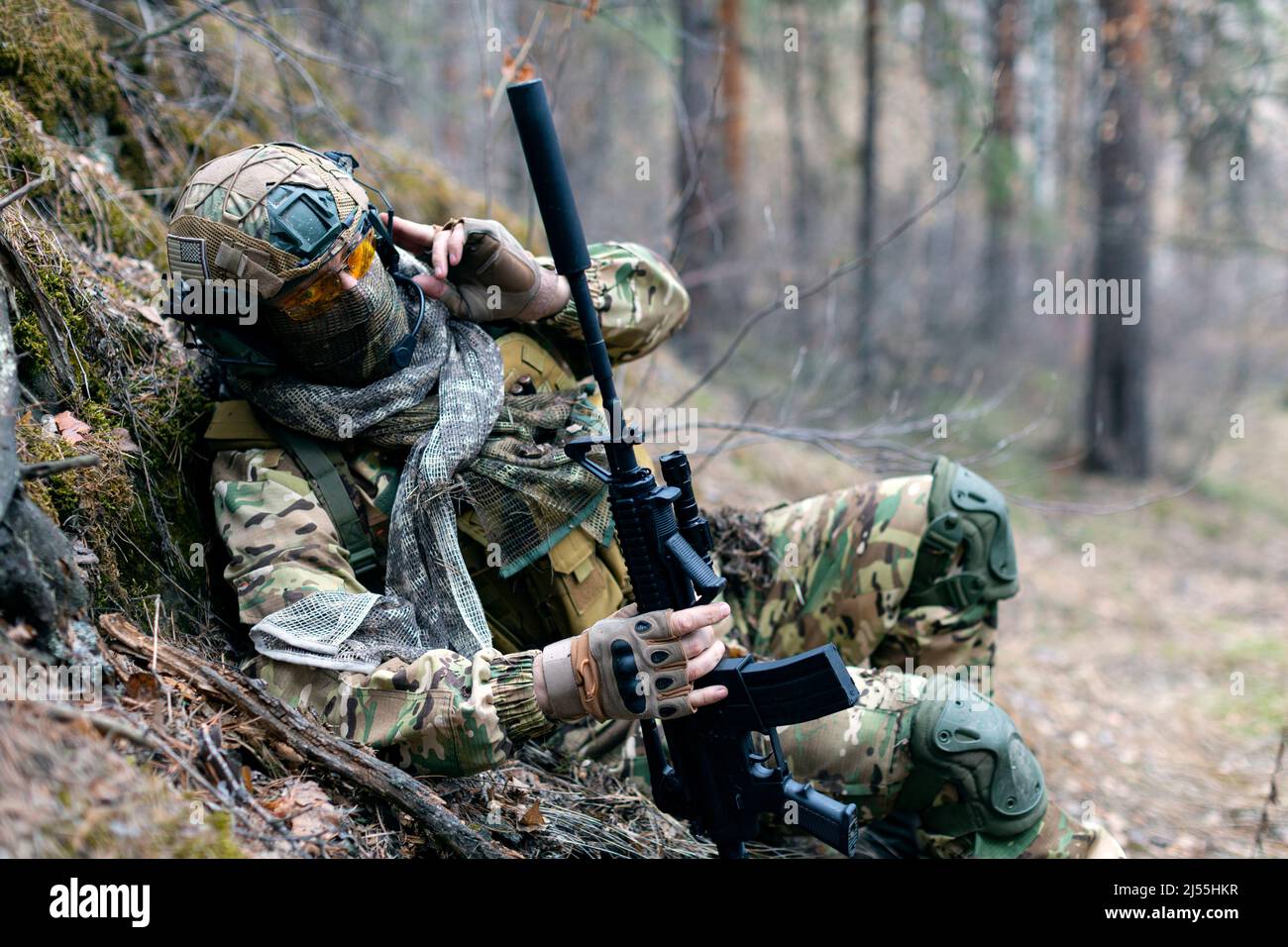 Photo of a special forces soldier during a clash in the forest. He calls his group's support on the walkie-talkie. The concept of modern military oper Stock Photo