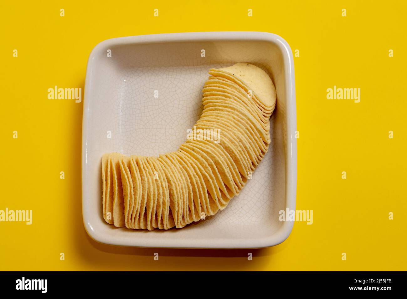 Stack of potato chips in a square serving bowl on yellow background Stock Photo