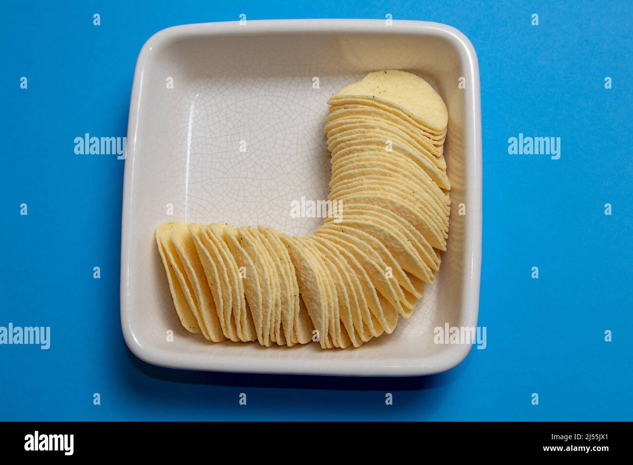 Stack of potato chips in a square serving bowl on blue background Stock Photo