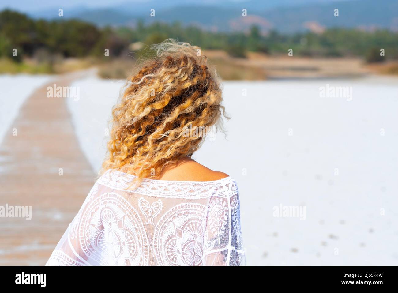 Back view of blonde surf waves hairstyle woman enjoying the beach in summer holiday vacation. Concept of tourist and tourism in the nature. Female peo Stock Photo