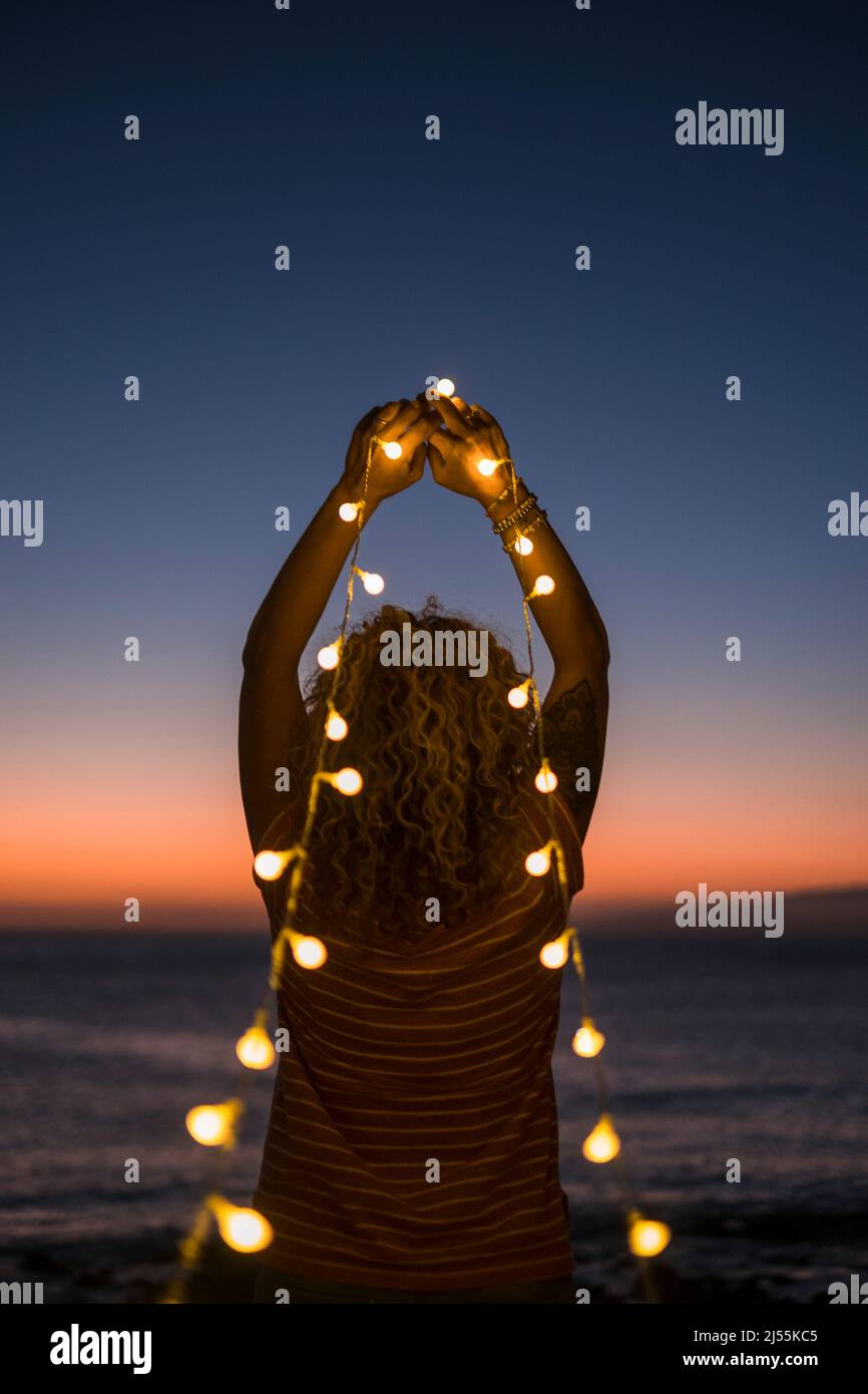 Concept of inner balance and happiness freedom life. Back view of woman admiring ocean sunset holding yellow bulb lights. Magic and mindfulness emotio Stock Photo