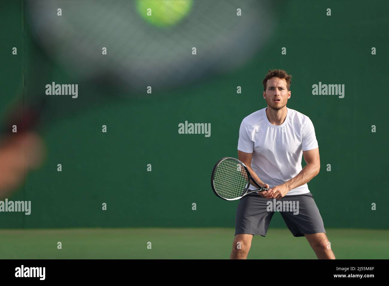 Tennis player focused on other player hitting ball with racket on court. Men sport athletes players playing tennis match together. Two professional Stock Photo