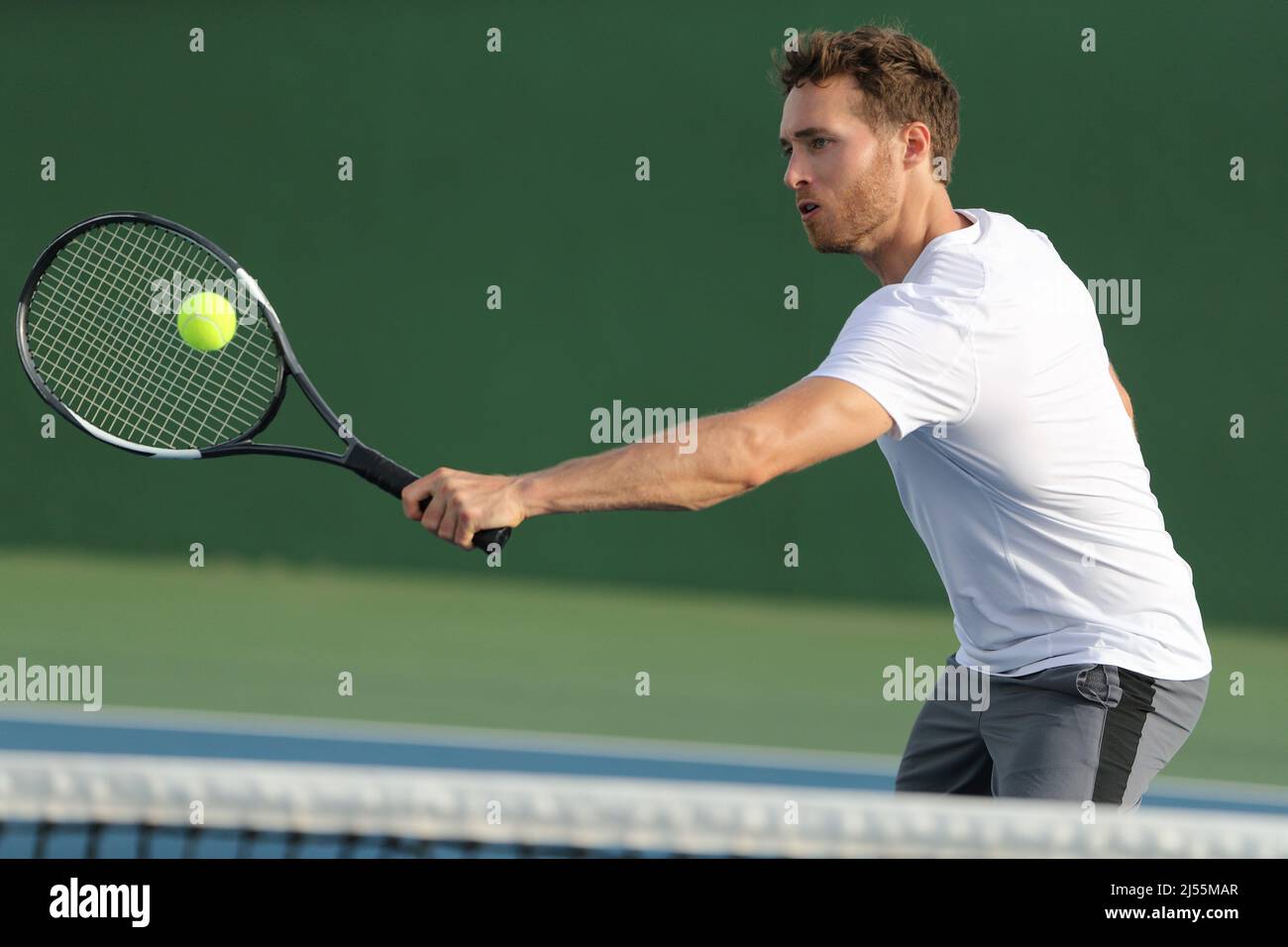 Tennis player hitting ball with backhand racket on hard court. Man playing game returning ball portrait Stock Photo